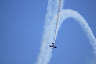 Low angle view of fighter plane performing smoking stunt against clear sky