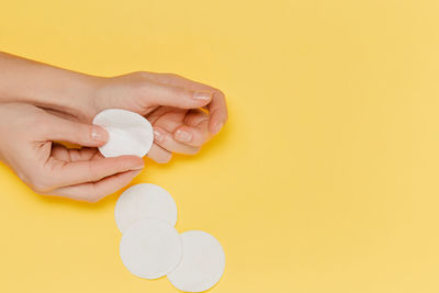 Cropped hand of woman holding dentures against yellow background