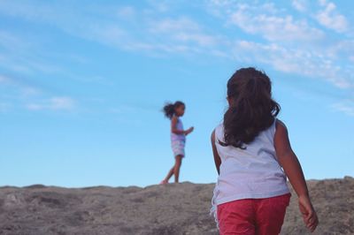 Rear view of girls walking on landscape against sky