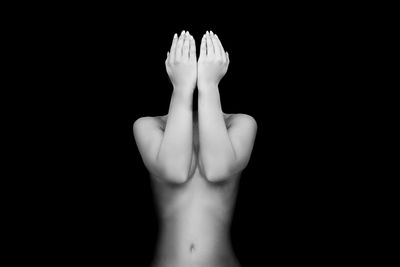 Shirtless young woman covering face against black background