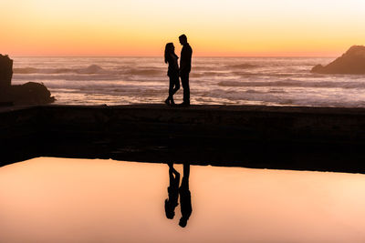 Silhouette couple on beach against sky during sunset