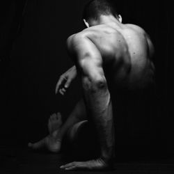 Rear view of shirtless man sitting against black background