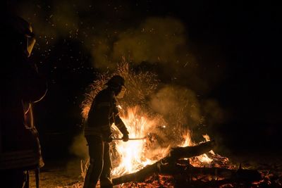 People standing by bonfire against sky at night