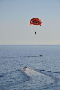 Person paragliding in sea against clear sky