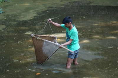 High angle view of man fishing with bamboo net while standing in pond