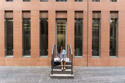 Businesswoman using laptop while sitting on steps at entrance of office building