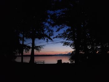 Silhouette trees by lake against sky during sunset