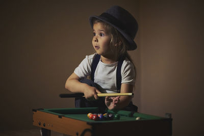 Charming child in retro clothes playing toy billiards.