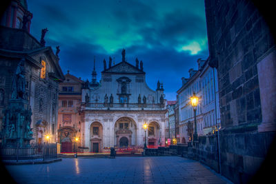 Illuminated street amidst buildings against sky at dusk