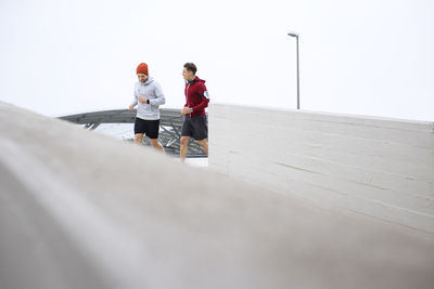 Male friends jogging on footpath at parking lot against clear sky