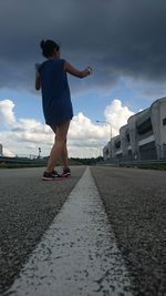 Rear view of woman standing on road against cloudy sky