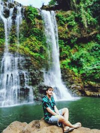 Man sitting on rock against waterfall in forest