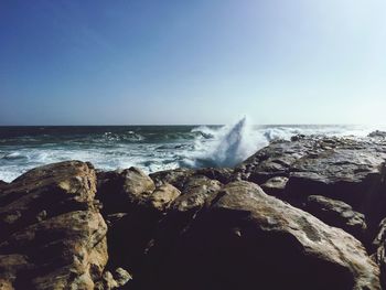 Waves splashing on rocks against clear blue sky