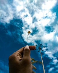 Close-up of hand holding kite string against blue sky