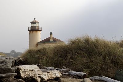 Lighthouse amidst rocks and buildings against sky