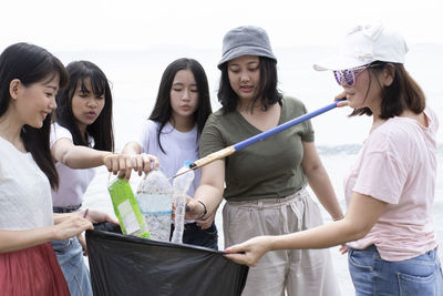 Friends collecting garbage while standing against sea