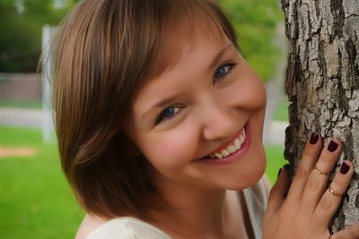 Close-up portrait of smiling woman by tree trunk