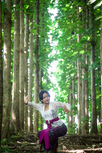 Full length of woman standing by tree in forest