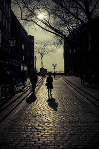 Silhouette person walking on footpath in city