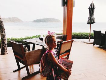 Woman sitting on table by sea against sky