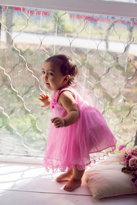 Girl child in pink dress sitting on the window on the white windowsill