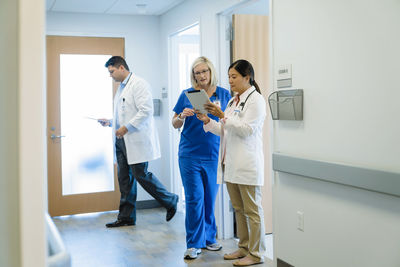 Female doctors discussing over tablet computer while male colleague walking by in hospital