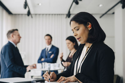 Female business person writing while standing at table in office workplace