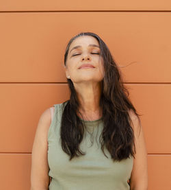 Woman with eyes closed leaning on orange wall