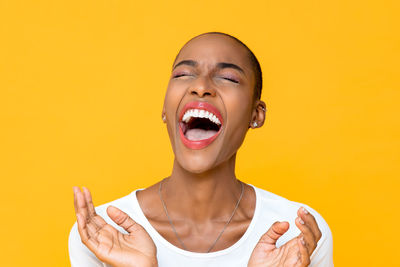 Close-up of woman with eyes closed laughing against yellow background