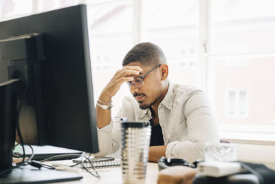 Computer programmer with head in hand sitting at desk by window in office