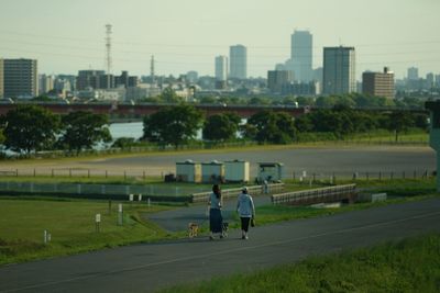 Rear view of people walking on road in city against sky