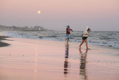 Women on beach against sky during sunset