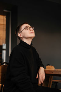 Young woman with short hair in eyeglasses and black sweater sitting at the table in office