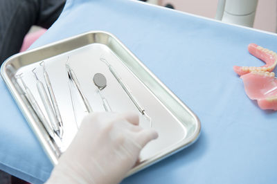 Cropped hand of dentist holding dental equipment in tray on table