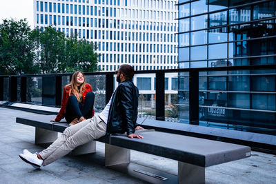 Young couple sitting on bench against buildings