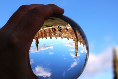 Close-up of hand holding crystal ball against blue sky