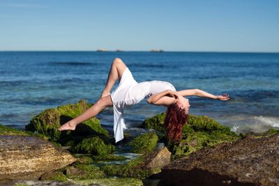 Woman levitating at beach against sky