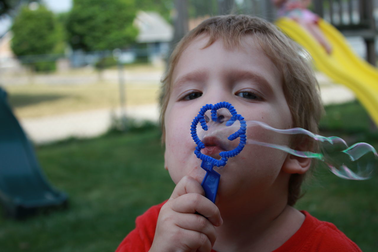 focus on foreground, real people, innocence, childhood, one person, girls, looking at camera, holding, lifestyles, leisure activity, close-up, grass, day, outdoors, bubble wand, finger in mouth