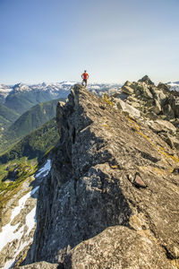 Trail runner stands on mountain summit, edge of a cliff.