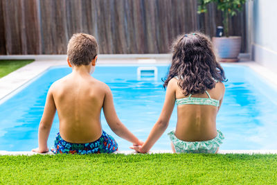 Two little kids on the edge of the swimming pool. rear view