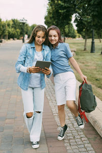 Two schoolgirls are holding a tablet in their hands and watching a video, laughing on the way 