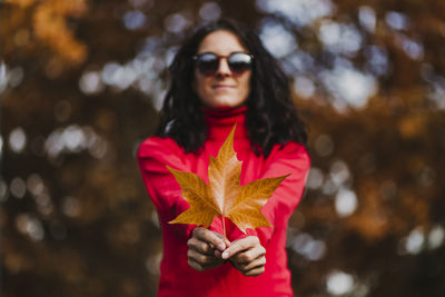 Portrait of beautiful young woman standing by maple leaf during autumn