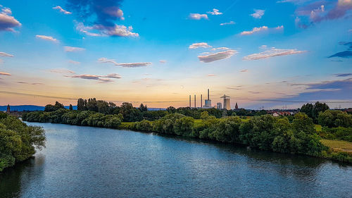 Scenic view of river by buildings against sky at sunset