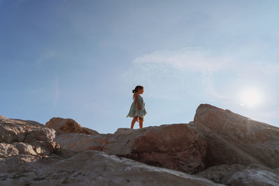 Rear view of girl standing on rock against sky