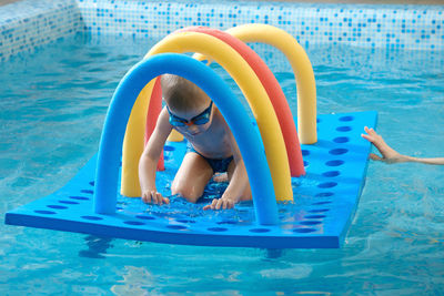 Toddler child crawling through tunnel on the water. kid learning to swim in swimming pool in goggles