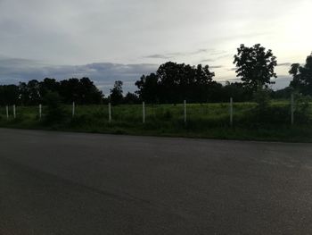 Road by trees on field against sky