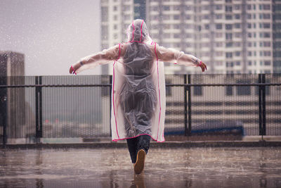 Full length rear view of woman with arms raised standing in rain