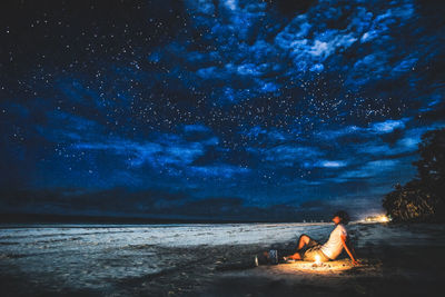 People sitting on beach against star field at night