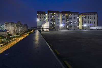 Illuminated road by buildings against sky at night