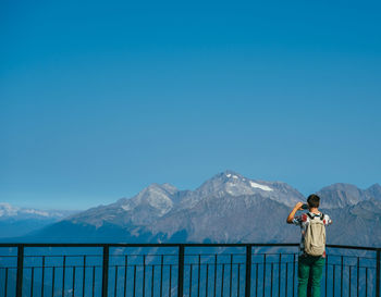 Rear view of man looking at mountains against clear blue sky